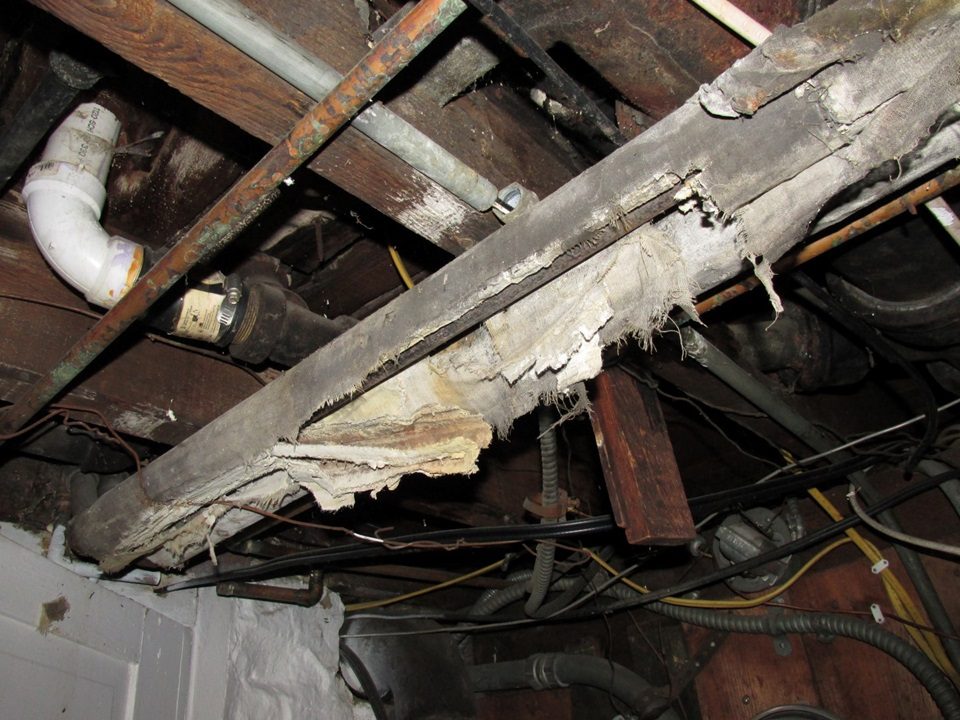 Deteriorating asbestos insulation wrap on a beam in an old basement ceiling