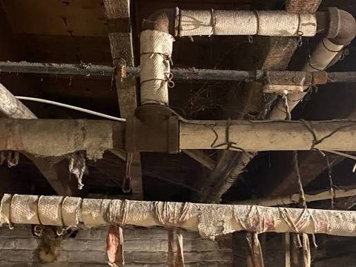 Aged asbestos pipe insulation on pipes under old floor joists
