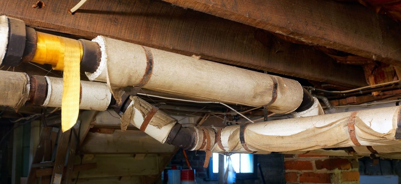 Asbestos cloth insulation wrap on heating pipes in a basement ceiling